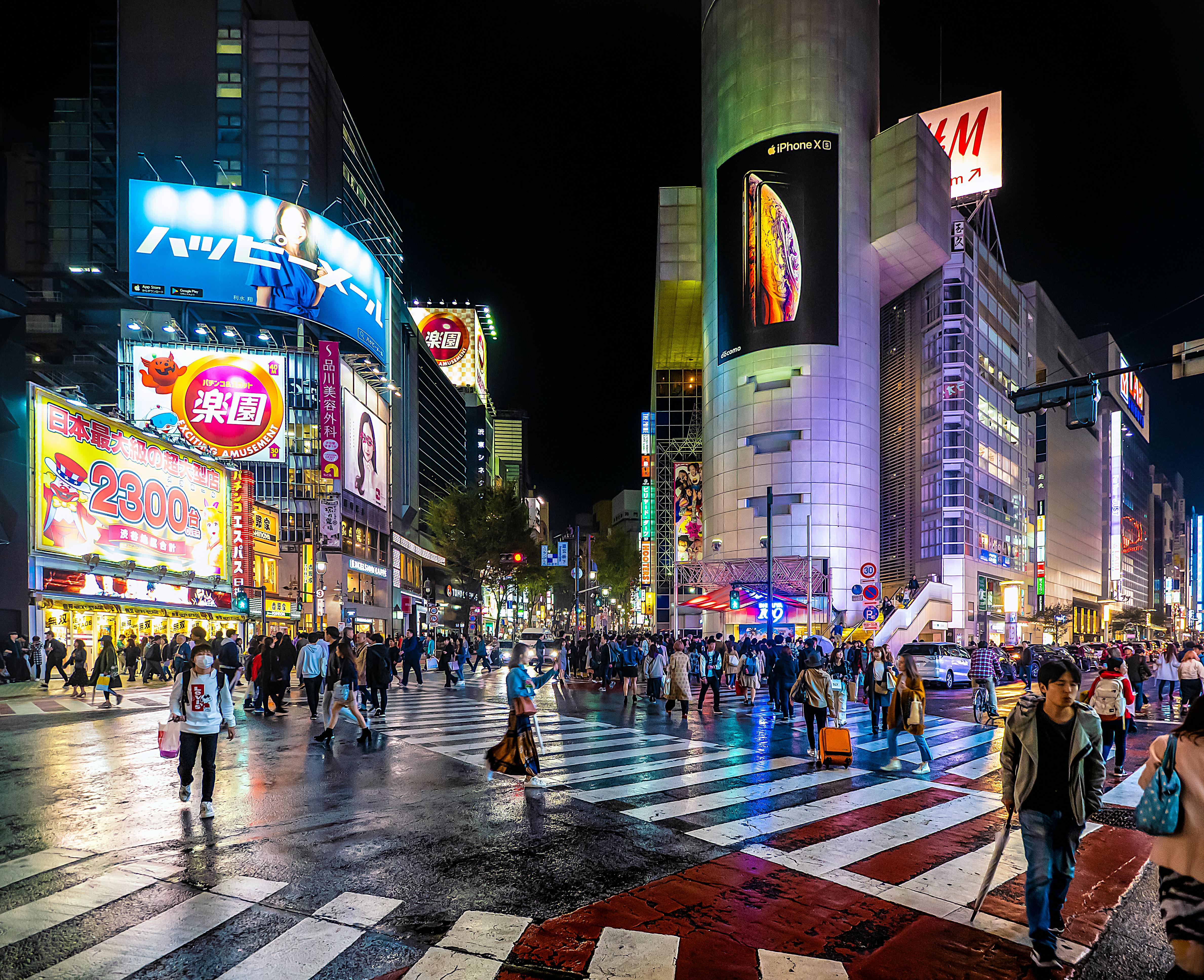 A bustling city street at night, filled with people walking and crossing the road under bright city lights