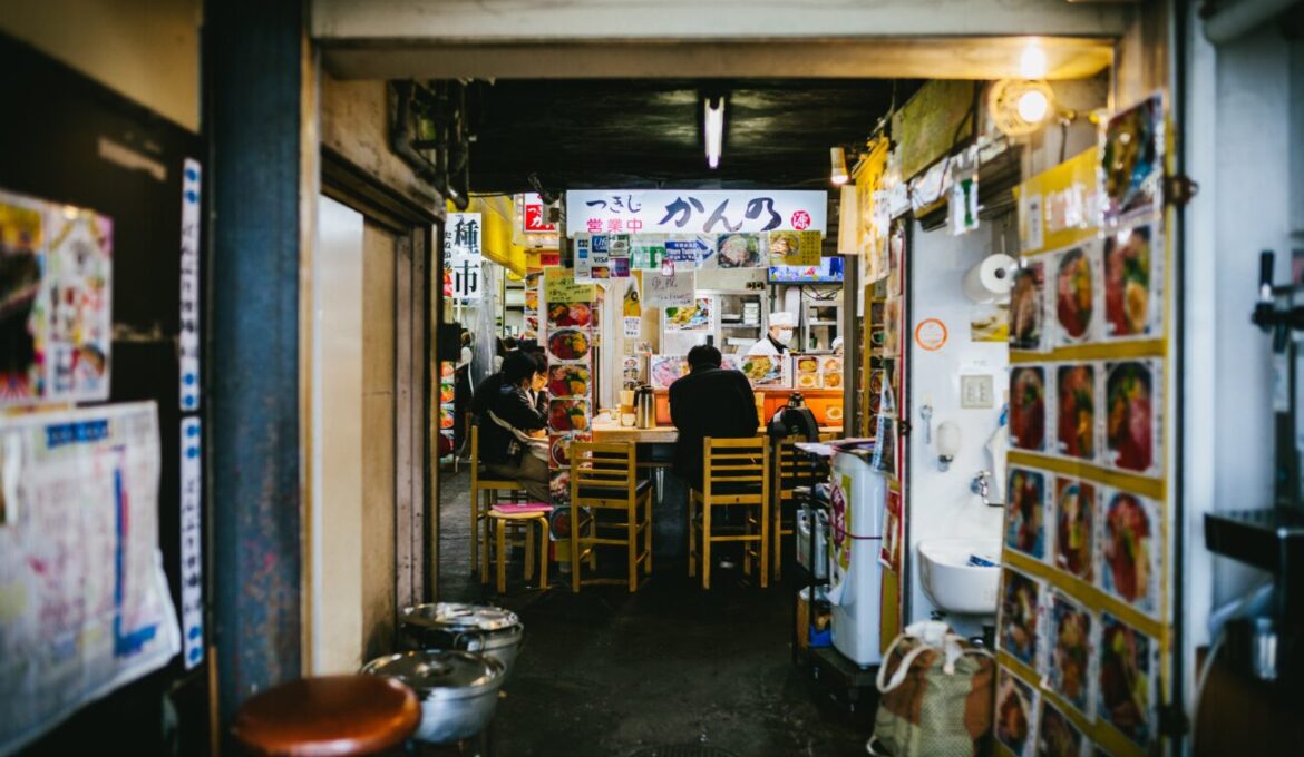 A narrow alleyway filled with people seated at tables, enjoying food and drinks in a lively outdoor setting