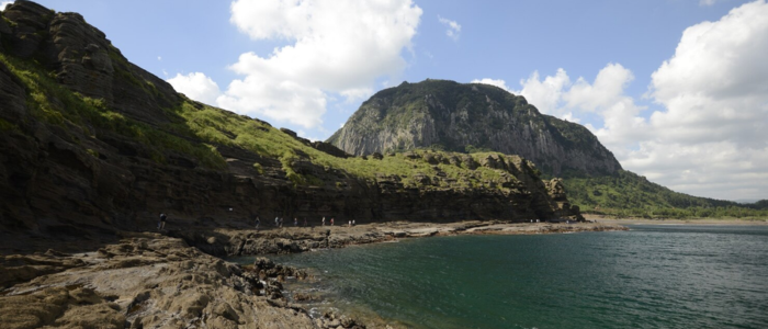 A rocky shore with a mountain rising majestically in the background under a clear blue sky.