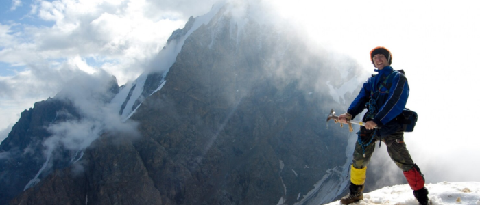 A man stands atop a mountain, wearing a backpack, gazing at the expansive landscape below.