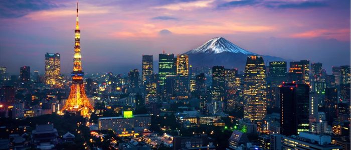 Night skyline of Tokyo with the illuminated Tokyo Tower and city lights under a twilight sky. Snow-capped Mount Fuji is visible in the background.