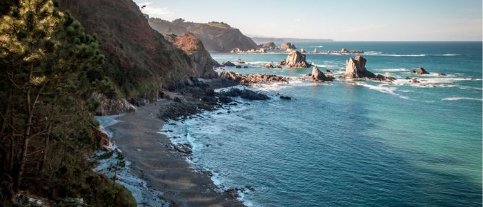 Coastal scenery with rugged cliffs and rocky formations extending into turquoise waves under a clear sky, evoking a serene and timeless atmosphere.